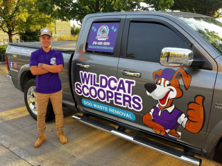 A person in a purple shirt and cap stands beside a parked truck featuring a cartoon dog and the text “Wildcat Scoopers: Dog Waste Removal” on the side. Trees and pavement are visible in the background. A person in a purple shirt and cap stands beside a parked truck featuring a cartoon dog and the text "Wildcat Scoopers: Dog Waste Removal" on the side. Trees and pavement are visible in the background.